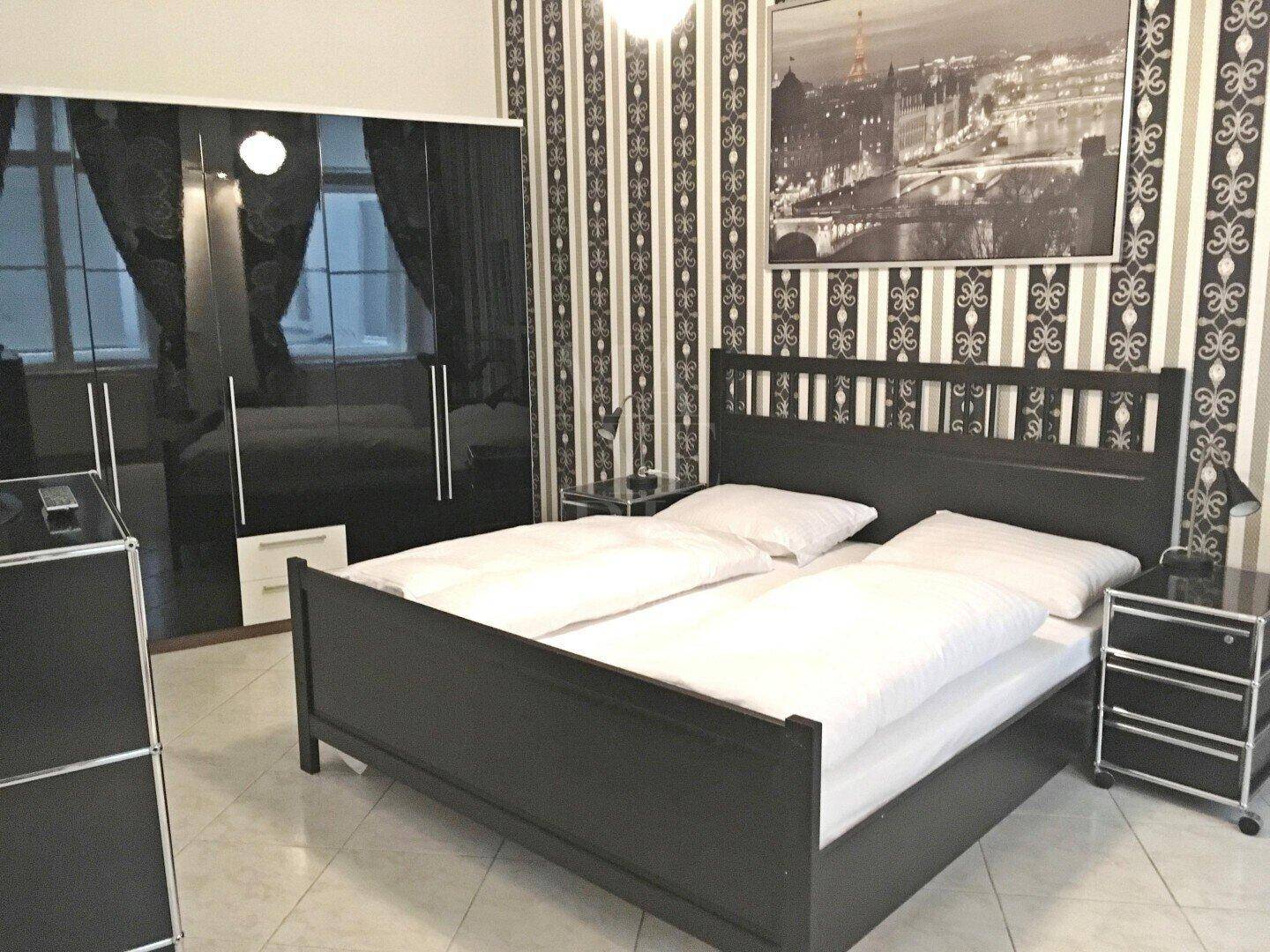 Schlafzimmer mit Doppelbett, schwarzem Kleiderschrank und auffälliger Tapete.