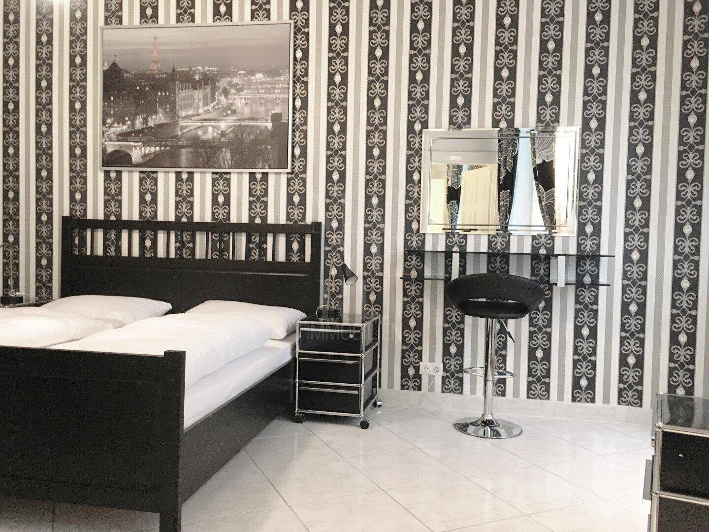 Schlafzimmer mit Doppelbett, Schminktisch und dekorativer schwarz-weißer Tapete.