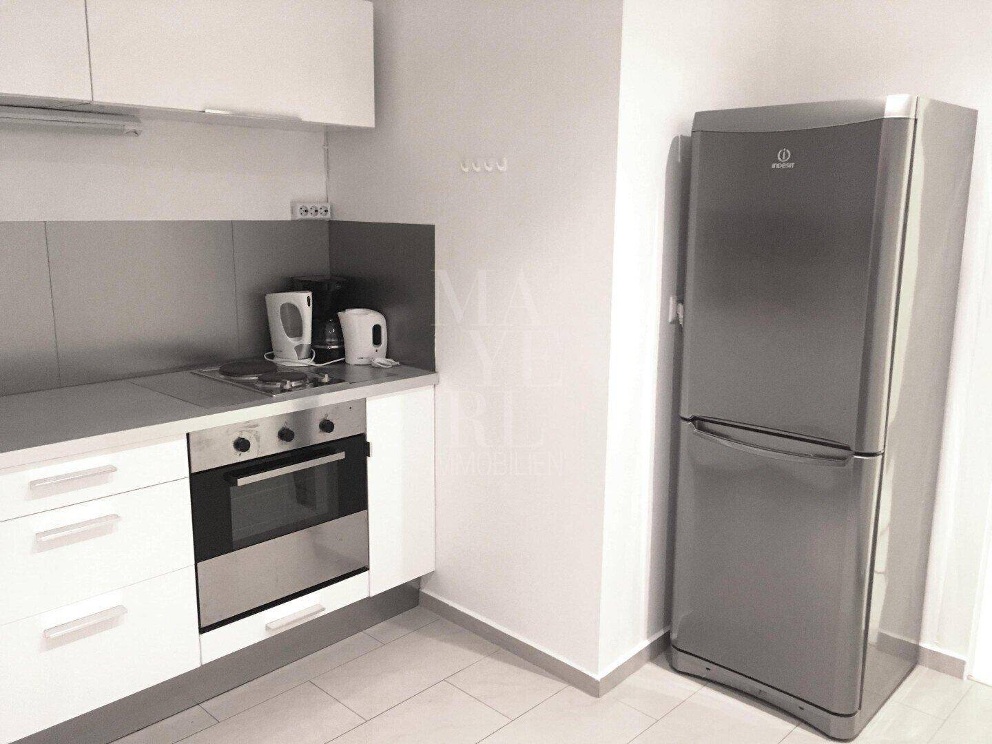 Küchenzeile mit Kühlschrank, Kochfeld und weißen Unterschränken.