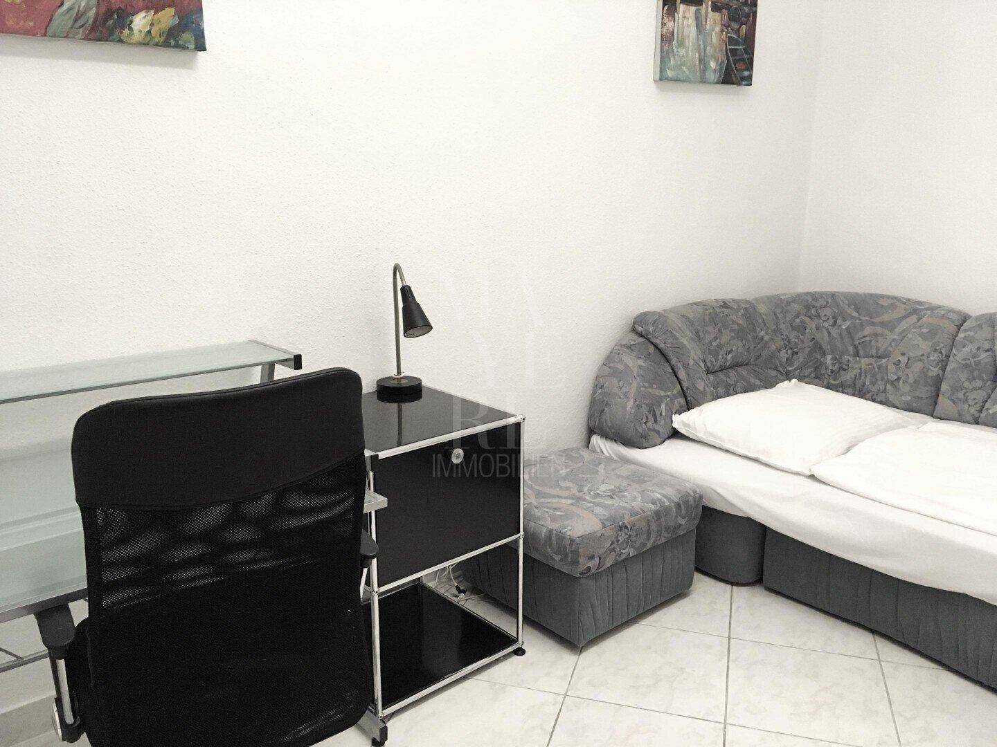 Arbeitszimmer mit Schreibtisch, Bürostuhl und einem Schlafsofa.