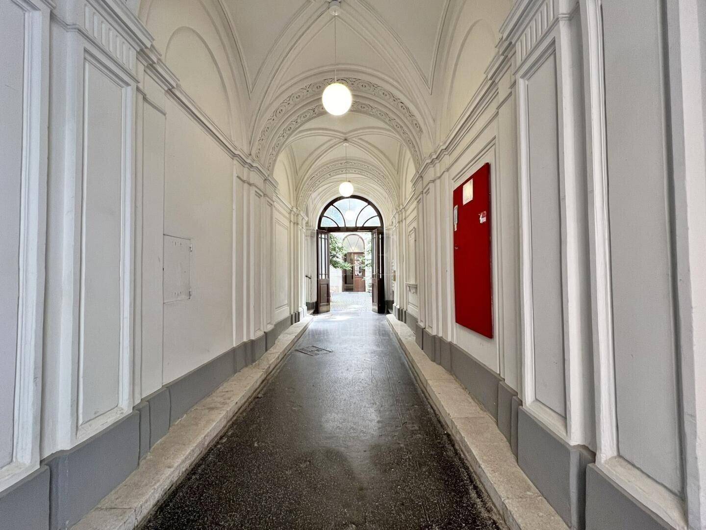 Ein langer, heller Durchgang mit einem beeindruckenden Gewölbedecke, der zu einem Innenhof führt.