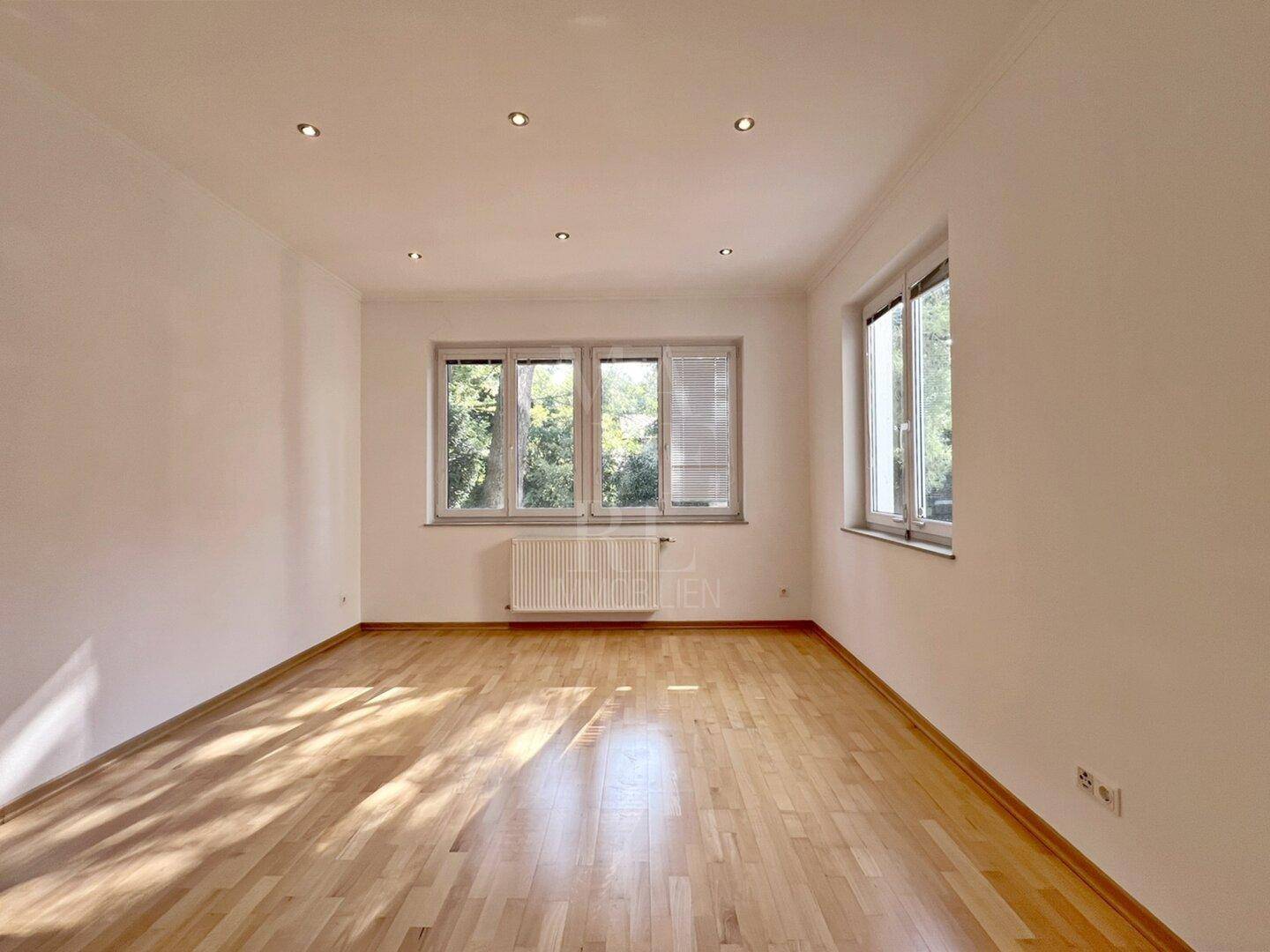 Helles Zimmer mit Parkettboden und mehreren Fenstern, die für eine angenehme Belichtung sorgen.
