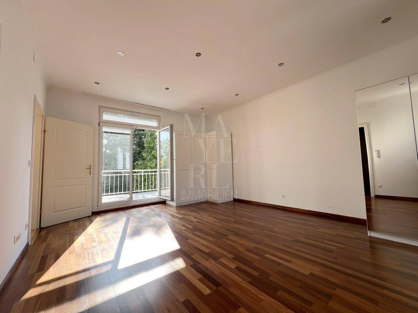 Schlafzimmer mit dunklem Parkettboden, Spiegelschrank und direktem Zugang zu einem Balkon.