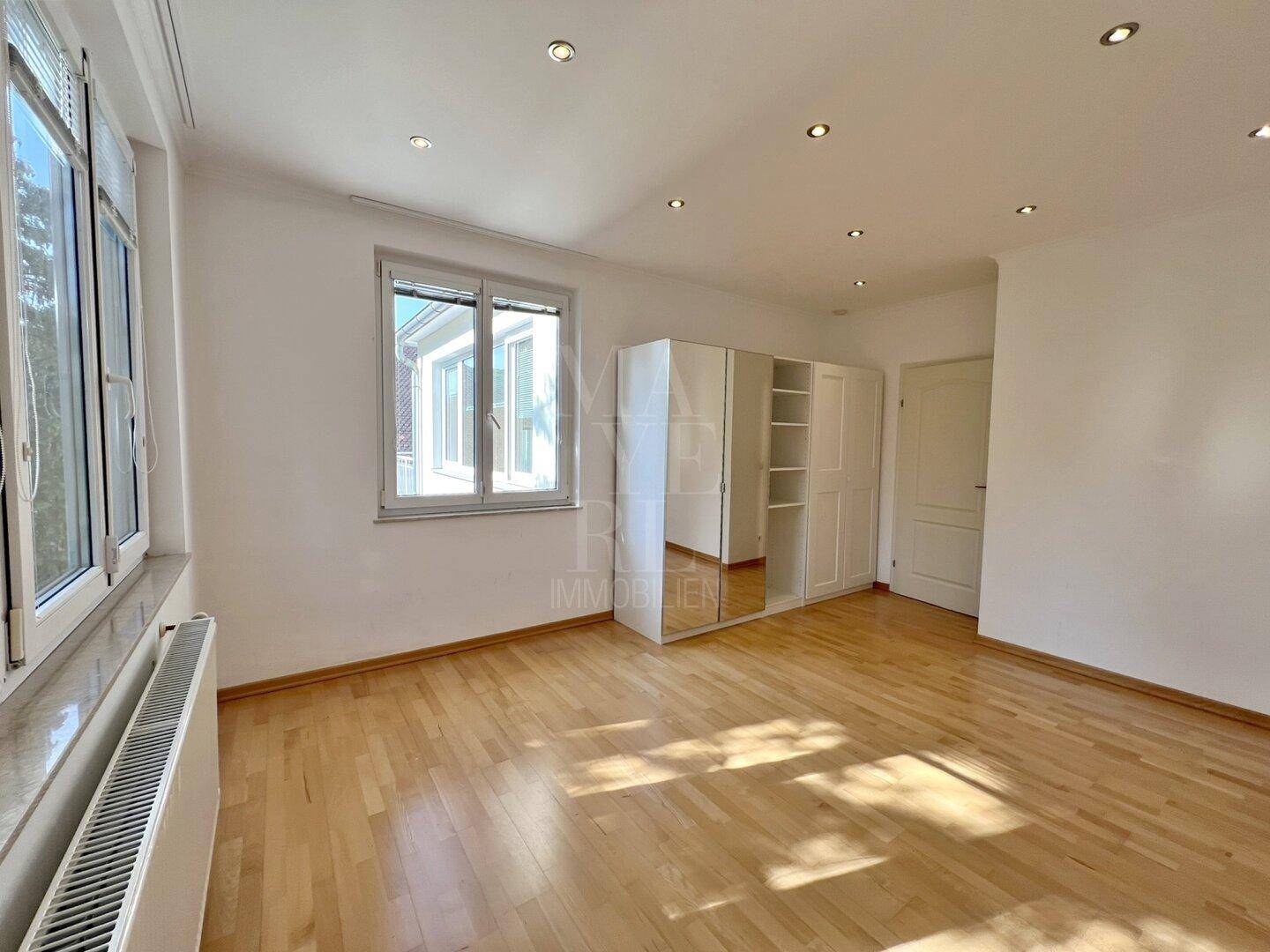 Helles Zimmer mit Parkettboden und Fenster, ausgestattet mit einem praktischen Kleiderschrank.