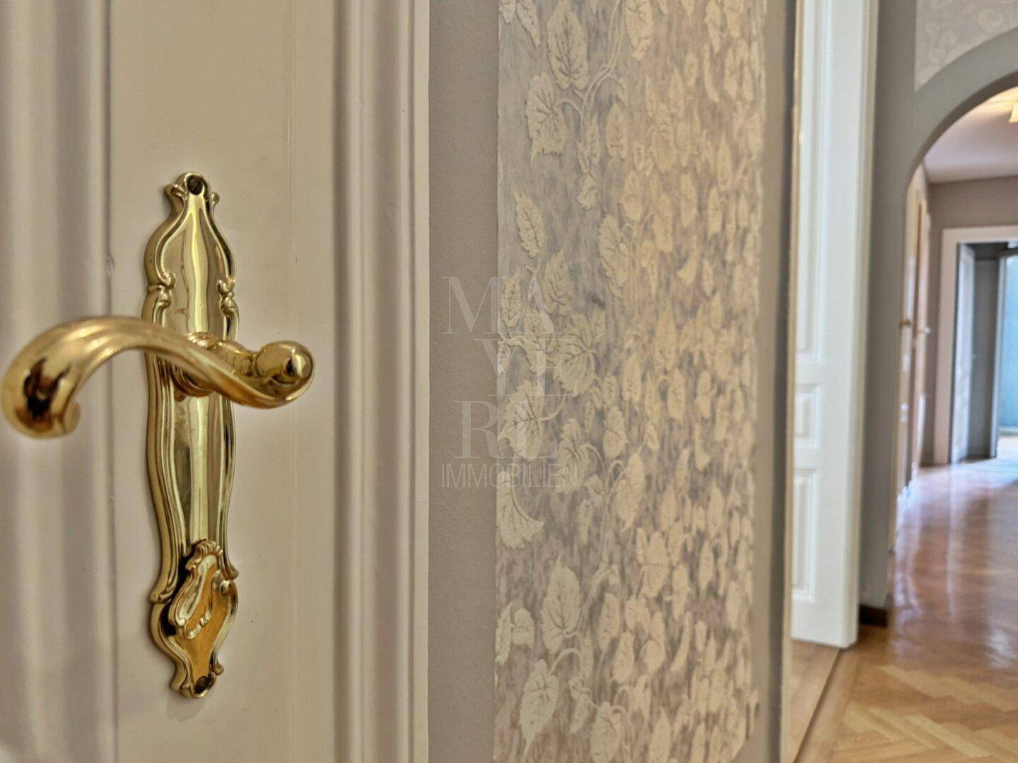 Detailaufnahme einer verzierten Tür mit goldener Klinke und dekorativer Tapete im Flurbereich.