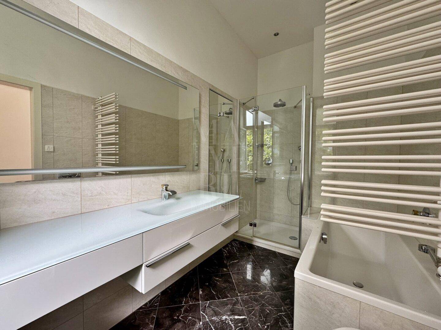 Modernes Badezimmer mit begehbarer Dusche, Badewanne, Doppelwaschbecken und dunklem Marmorboden.