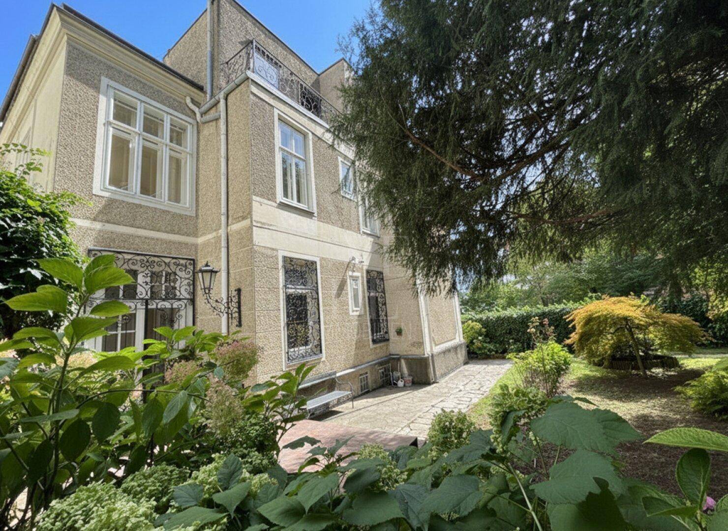 Gepflegter Gartenbereich mit altem Baumbestand und einem kleinen Sitzbereich neben der Villa.
