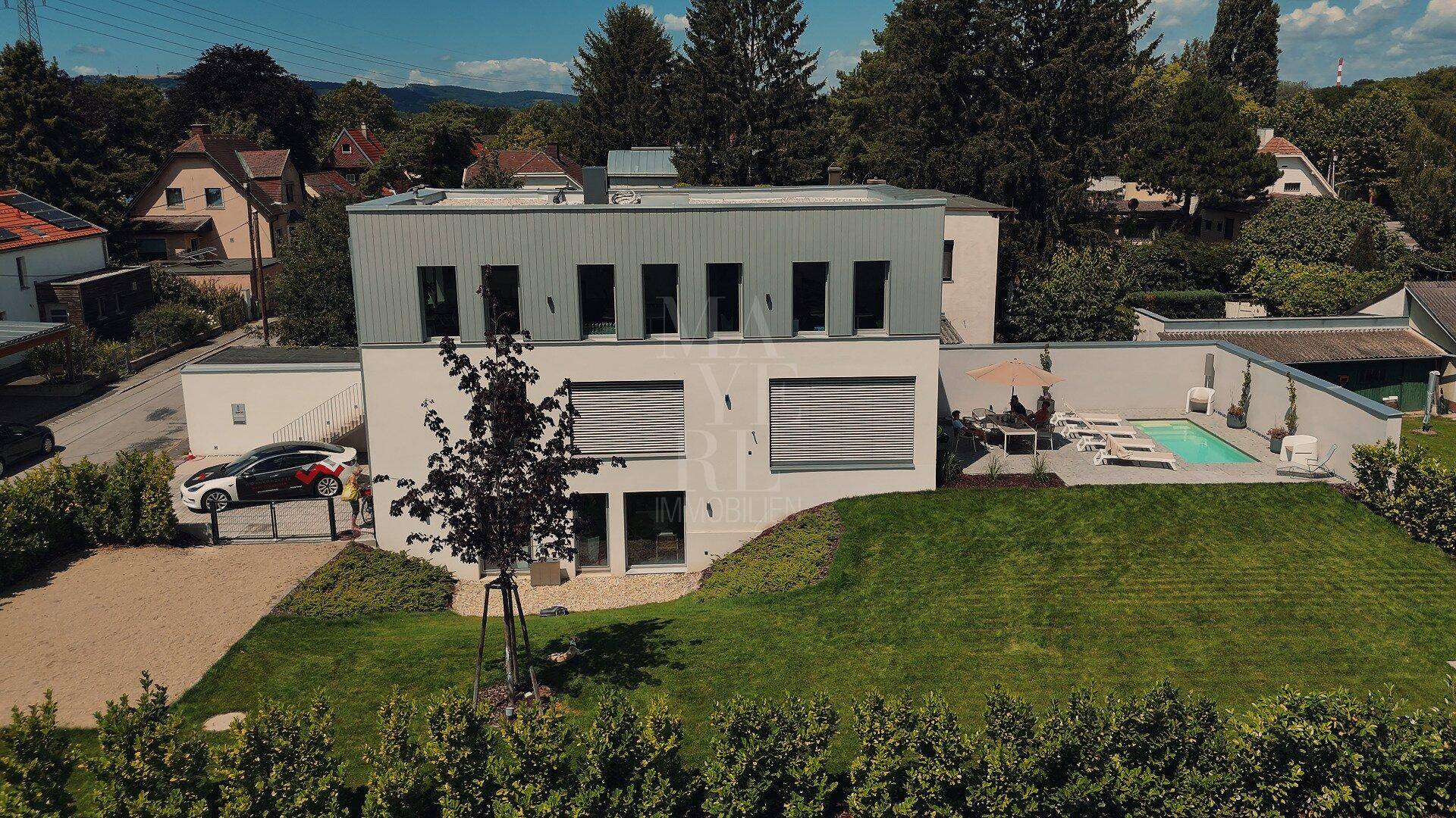 Ansicht des modernen Hauses mit Garten, Terrasse, Pool und Parkplatz für Fahrzeuge.