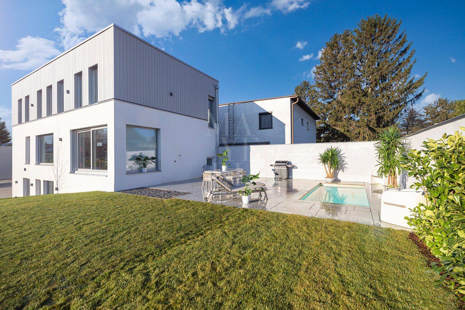Außenansicht des modernen Hauses mit gepflegtem Rasen, Terrasse und kleinem Poolbereich.