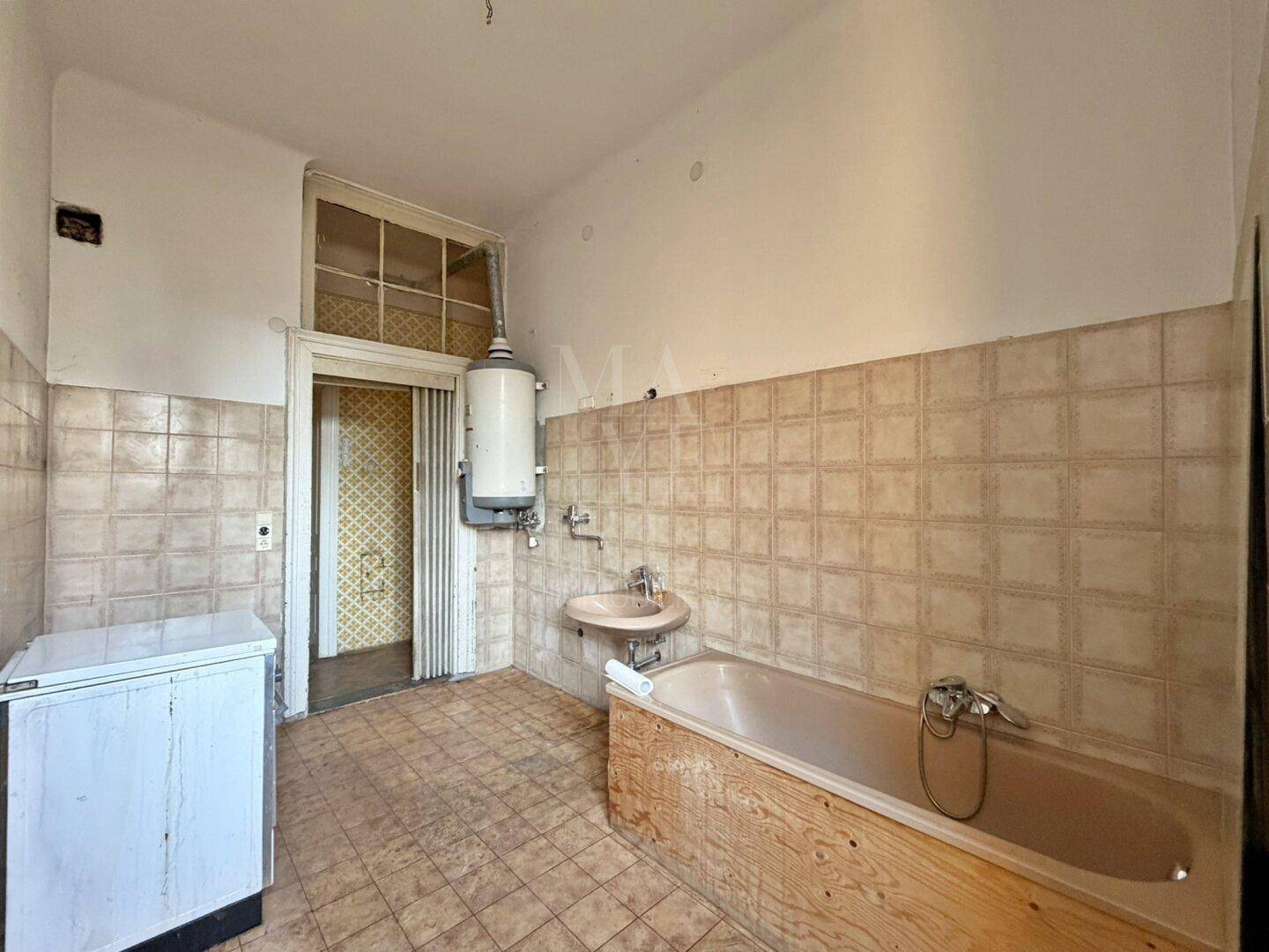 Badezimmer mit Badewanne, Waschbecken und Boiler, das eine umfassende Renovierung benötigt.