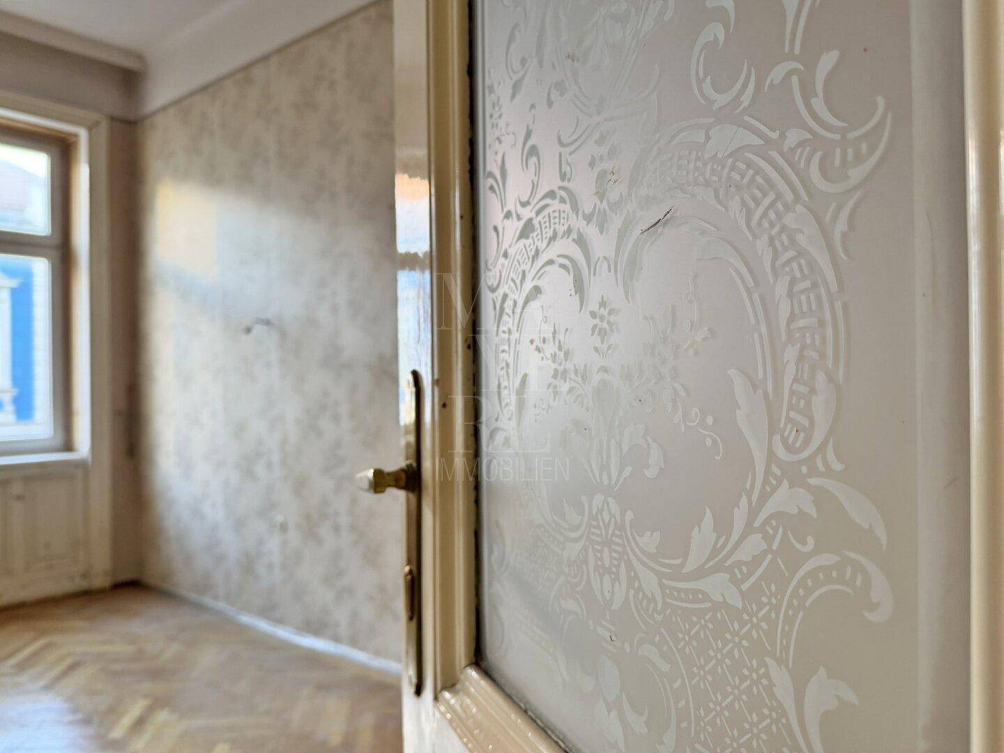 Detailaufnahme einer Tür mit dekorativem Glasmuster in einem Altbauflur.