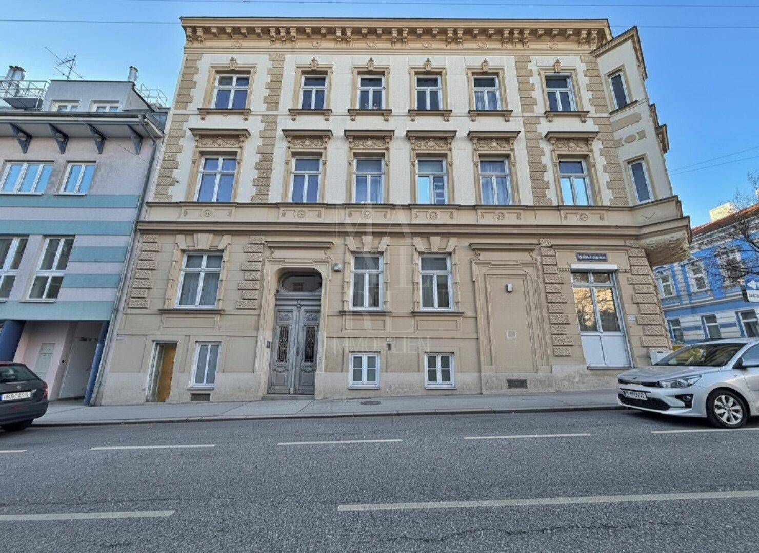 Historische Fassade eines Altbaus mit vielen Fenstern und dekorativen Elementen an einer Straße.
