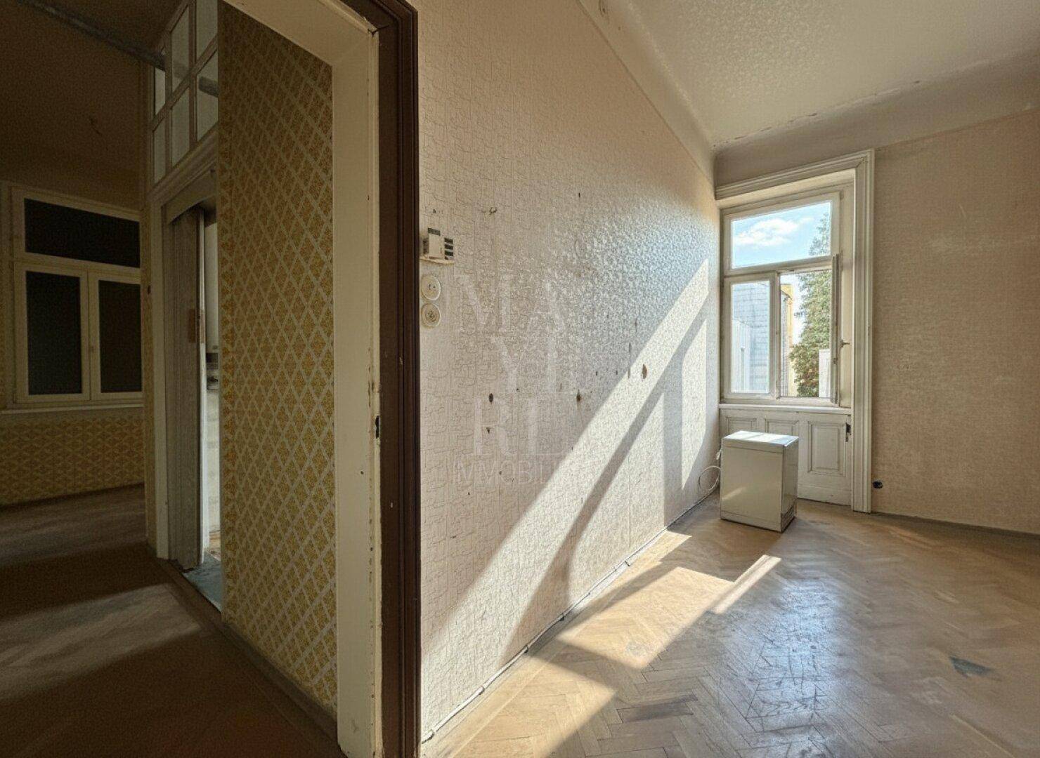 Heller Flur mit Fischgrätparkett und Fenstern, die Tageslicht hereinlassen.