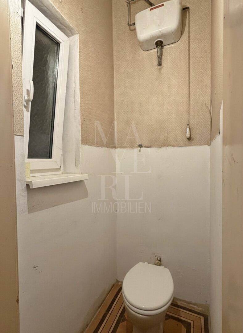Kleines WC mit Fenster und traditioneller Spülung, das eine Modernisierung erfordert.