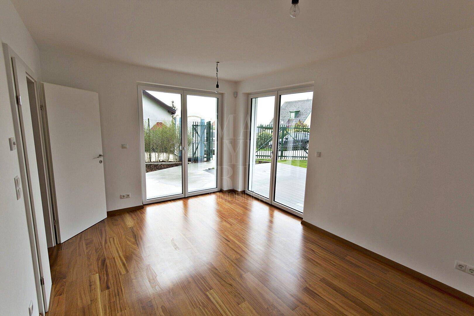 Heller Raum mit Holzboden und großen Fenstern, die viel Tageslicht hereinlassen.