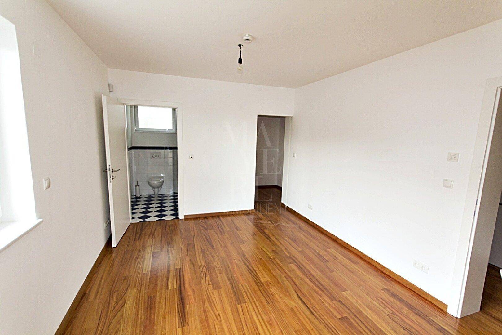 Geräumiger Raum mit Holzboden und direktem Zugang zu einem Badezimmer mit Fliesen.