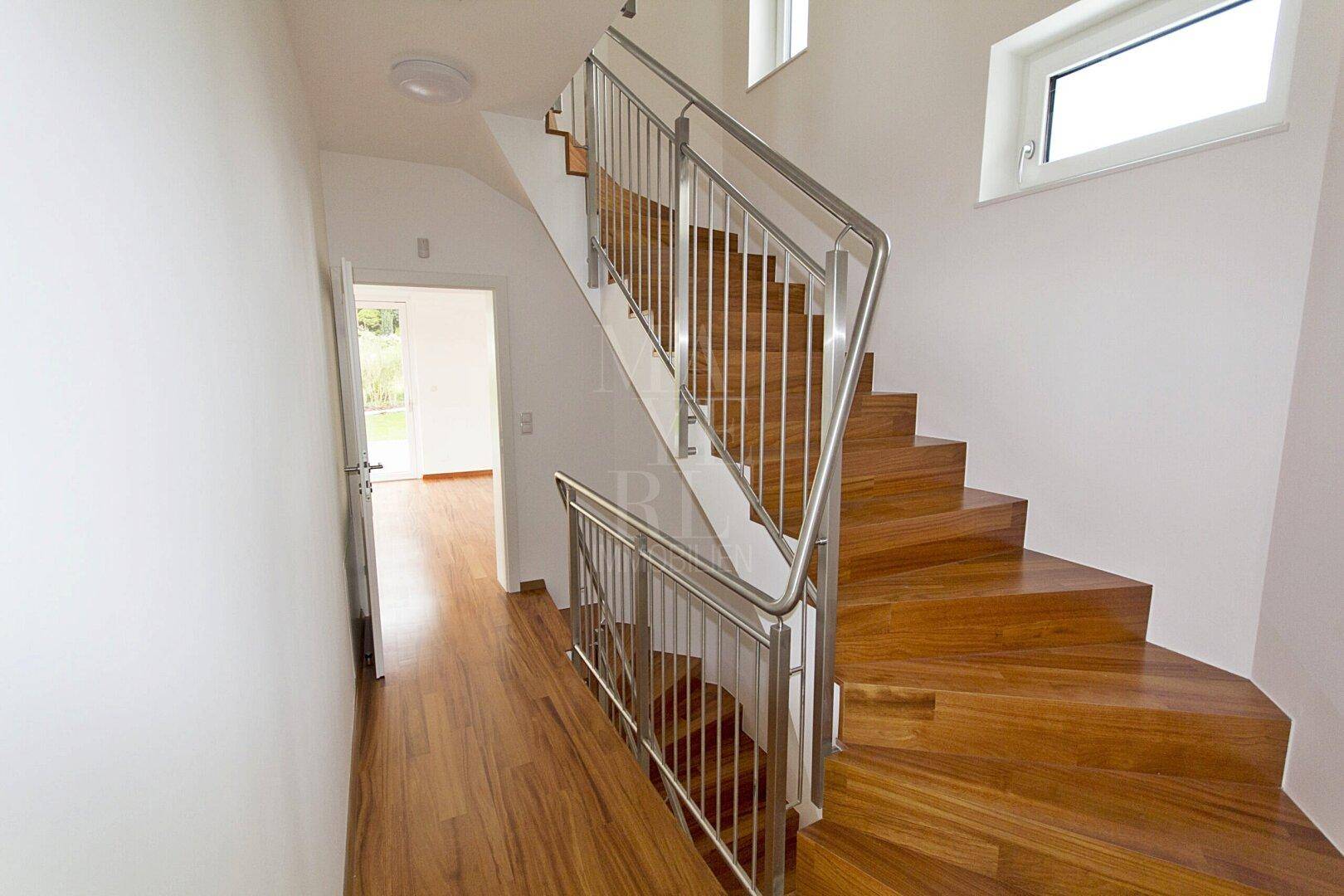 Moderner Flur mit eleganter Holztreppe und Edelstahlgeländer, der die Etagen verbindet.