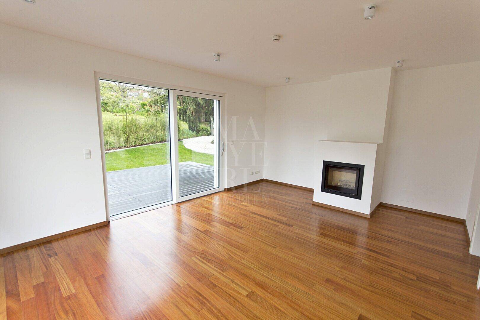 Helles Wohnzimmer mit Holzboden, integriertem Kamin und großen Schiebetüren zur Terrasse.