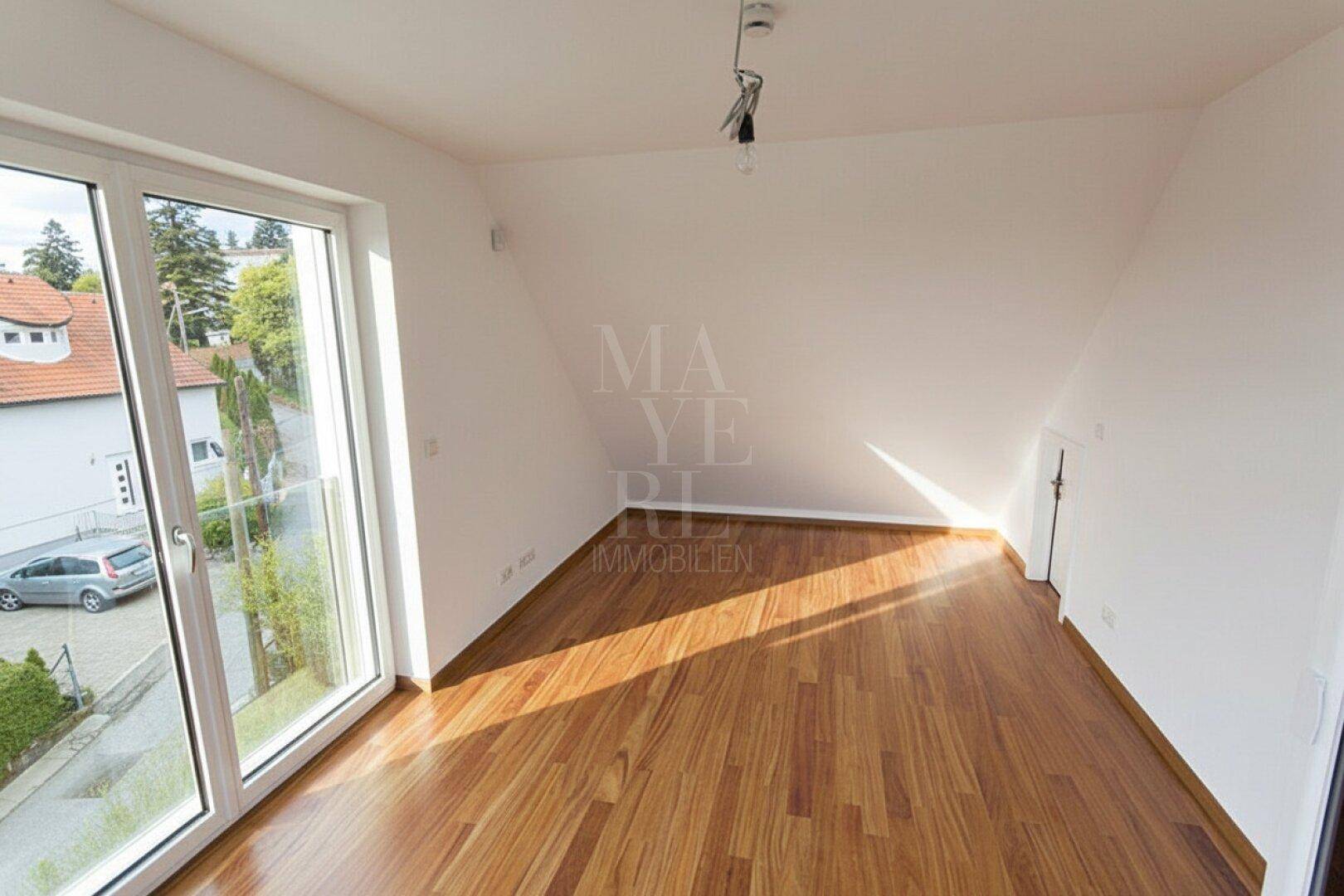 Lichtdurchfluteter Raum im Dachgeschoss mit Holzboden und schrägen Wänden, ideal als Schlafzimmer.