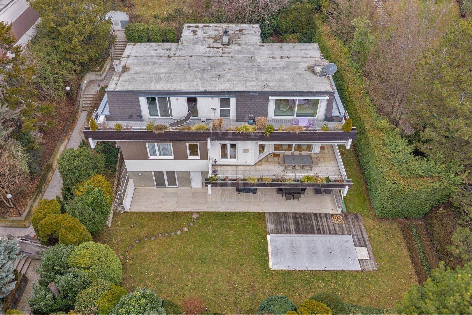 Luftaufnahme eines modernen Hauses mit mehreren Terrassen und einem gepflegten Gartenbereich.