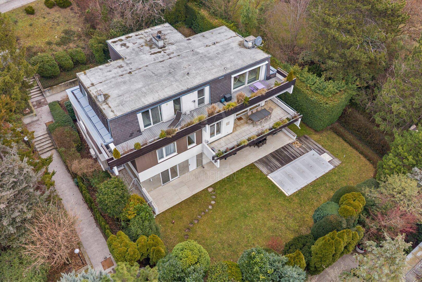 Luftaufnahme eines modernen Hauses mit mehreren Terrassen, Garten und Poolbereich.
