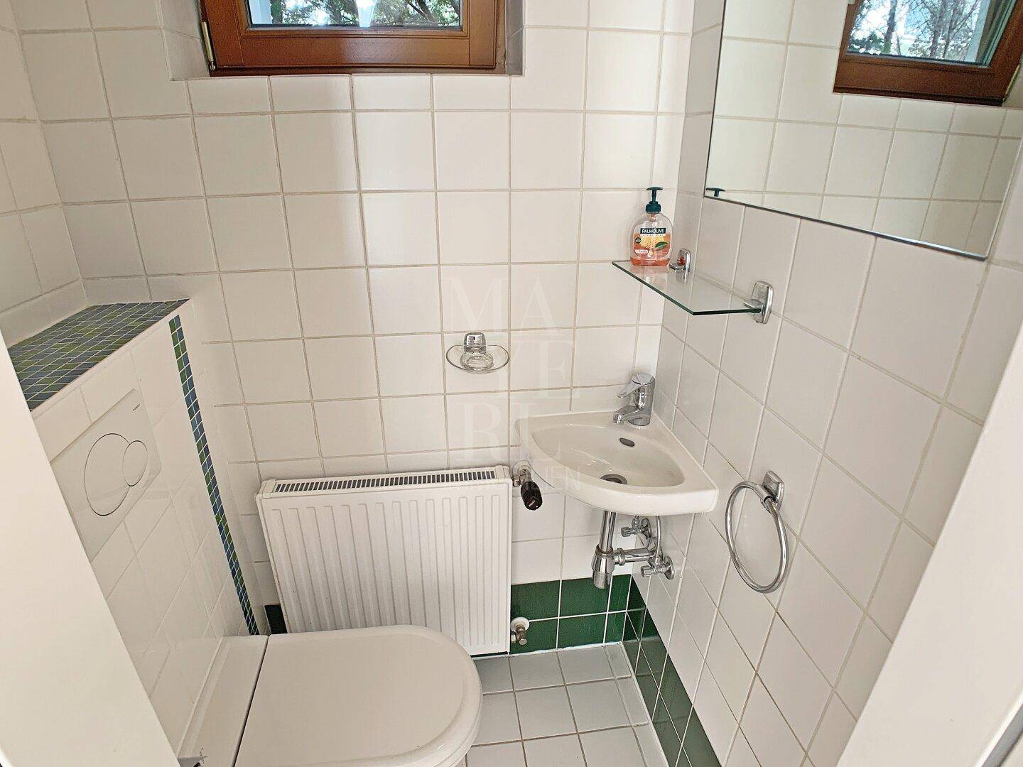 Kleines Gäste-WC mit Eckwaschbecken, Toilette und weißen Fliesen mit grünen Akzenten.