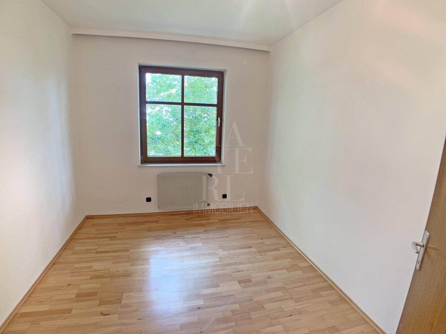 Ruhiges Schlafzimmer mit Holzboden und Fenster, das einen Blick ins Grüne bietet.