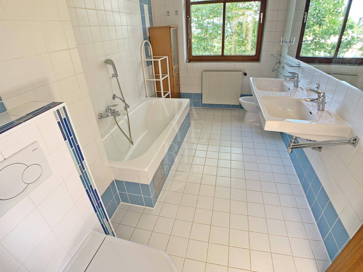 Geräumiges Badezimmer mit Doppelwaschbecken, Badewanne und blauen Akzentfliesen.