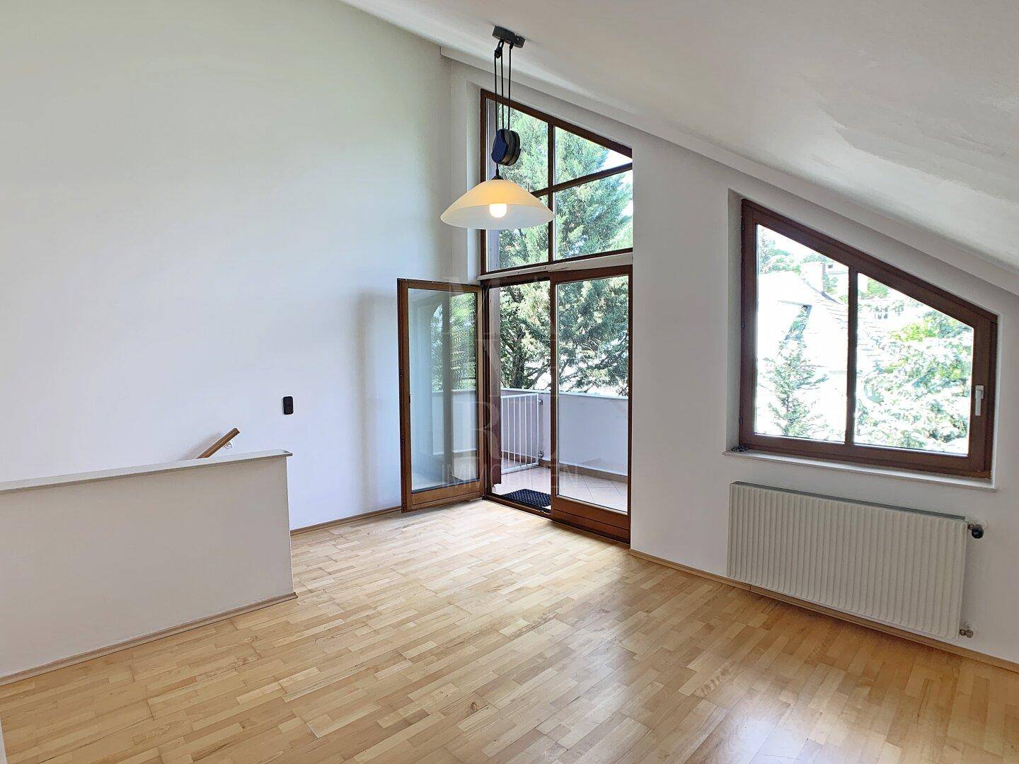 Heller Dachbodenraum mit hohen Decken, Parkettboden und Zugang zu einem Balkon.