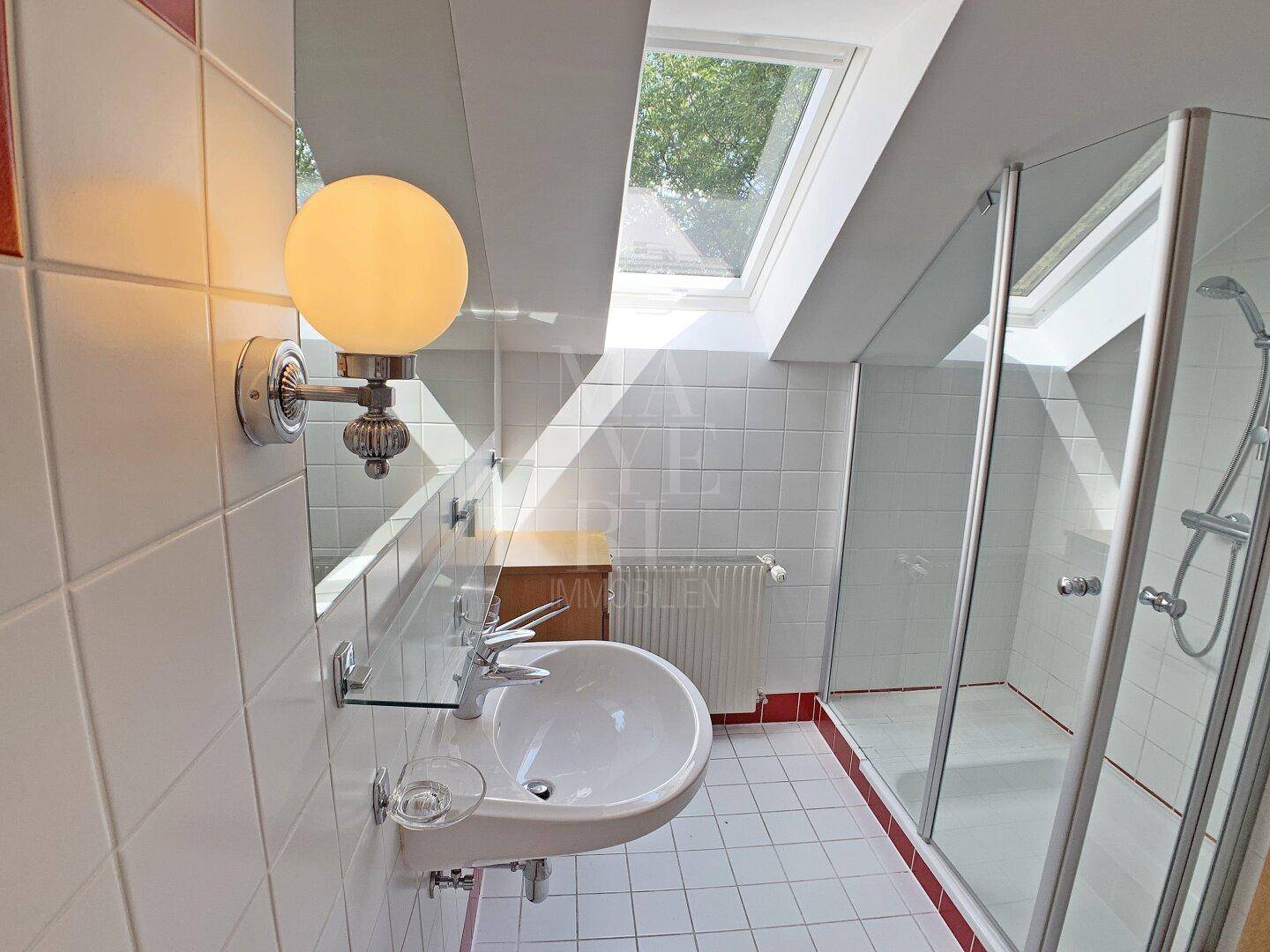 Badezimmer im Dachgeschoss mit Duschkabine, Einzelwaschbecken und Dachfenster für Tageslicht.