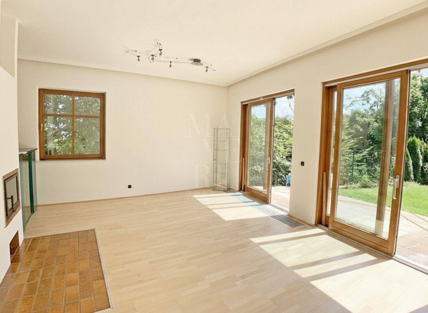 Helles Wohnzimmer mit Parkettboden, Kamin und großen Schiebetüren zum Garten.