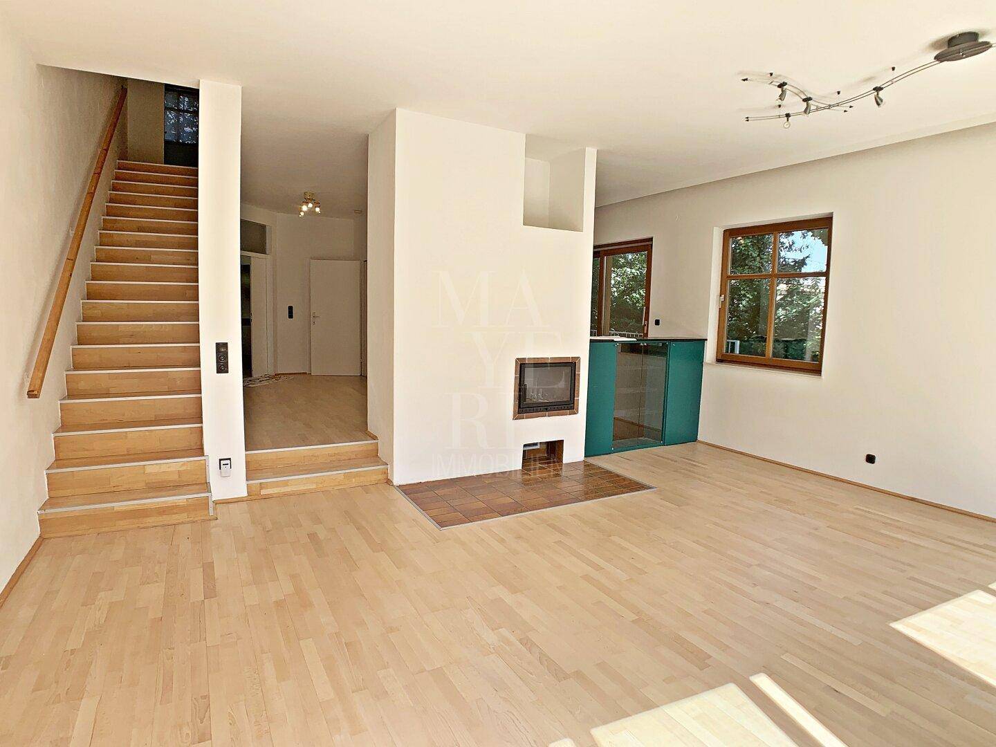 Geräumiges Wohnzimmer mit Kamin, Holztreppe und hellem Parkettboden, offen gestaltet.