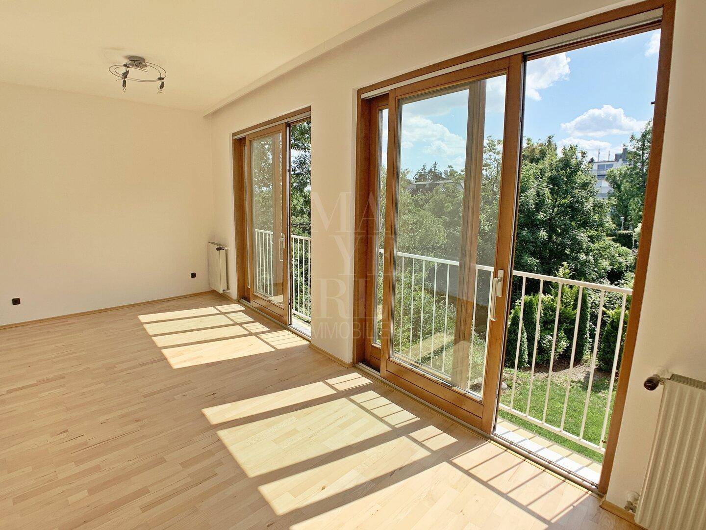 Helles Wohnzimmer mit Parkettboden und zwei französischen Balkonen mit Blick ins Grüne.