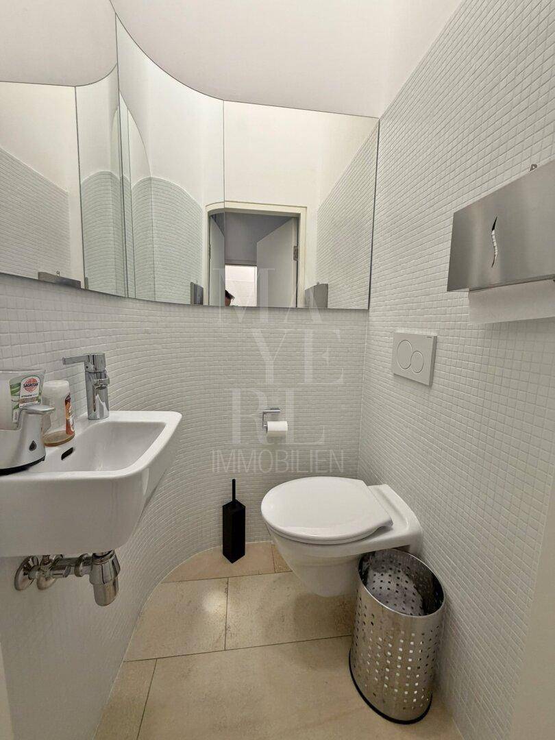 Moderne Toilette mit Mosaikfliesen, wandhängendem WC und kleinem Waschbecken.
