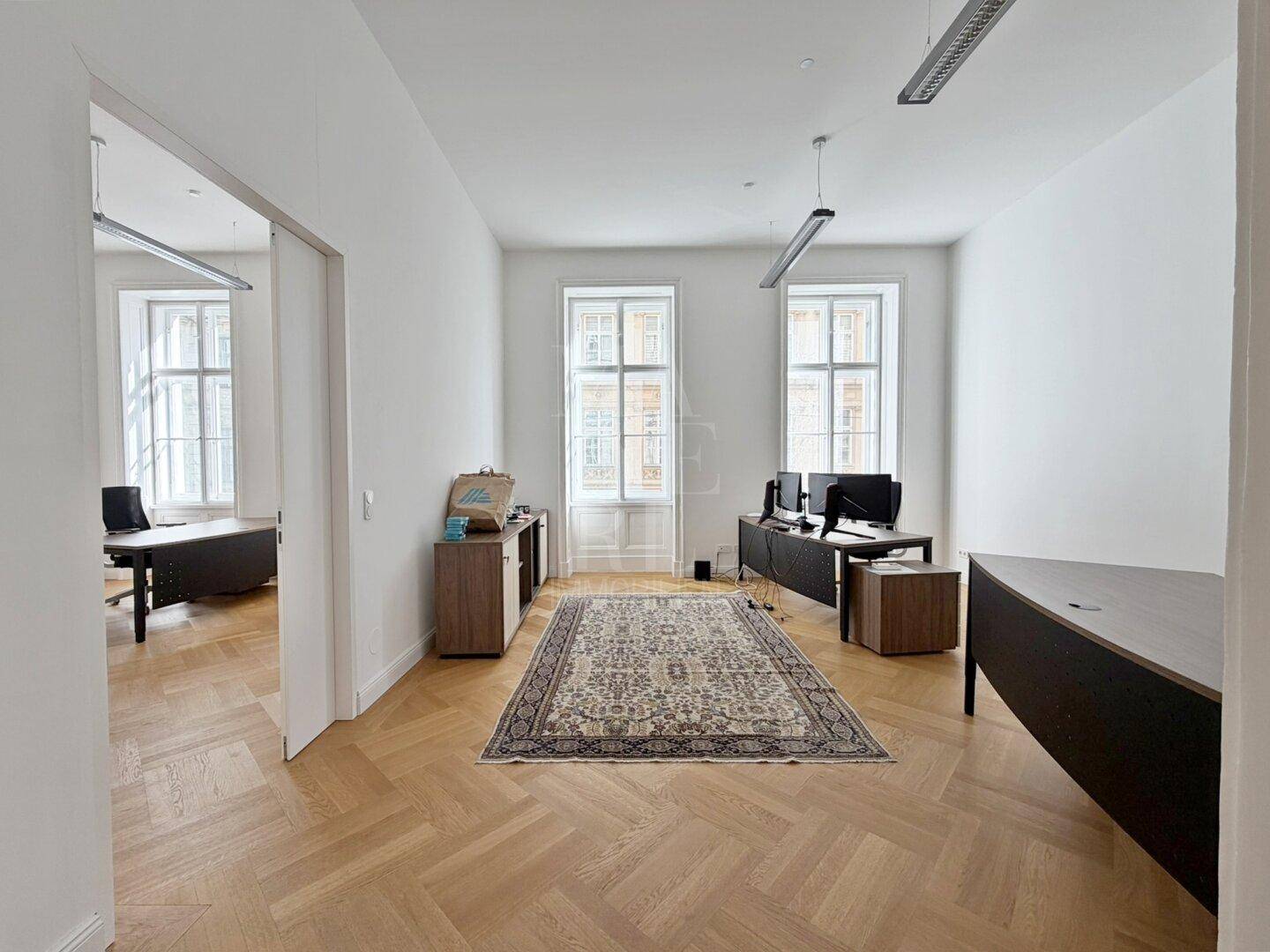 Geräumiges Büro mit Fischgrätparkett, großen Fenstern und Blick auf die Stadt.