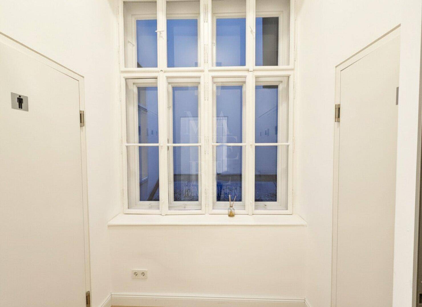 Heller Flur mit großem Fenster und Türen zu den Toilettenbereichen.