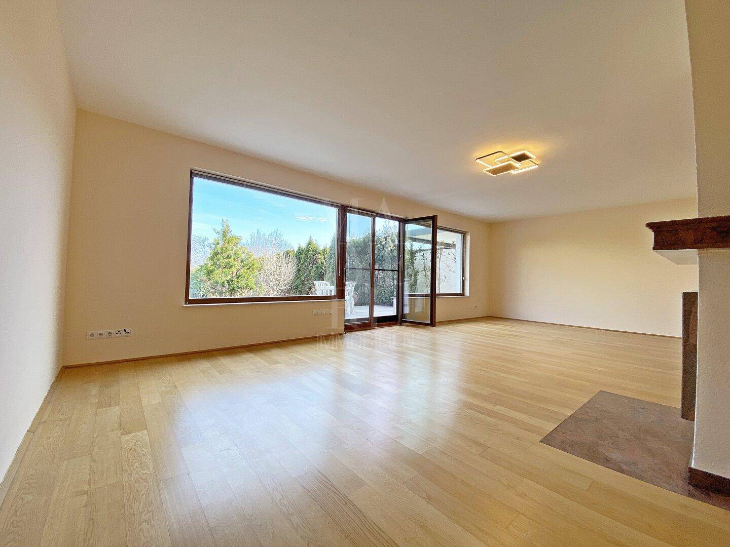 Helles Wohnzimmer mit Parkettboden und großen Fenstern, die viel Tageslicht hereinlassen.