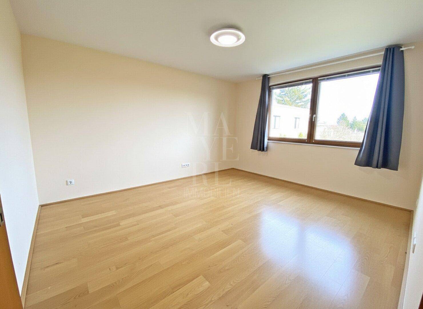 Helles Schlafzimmer mit Parkettboden und Fenster, das einen Blick ins Grüne bietet.