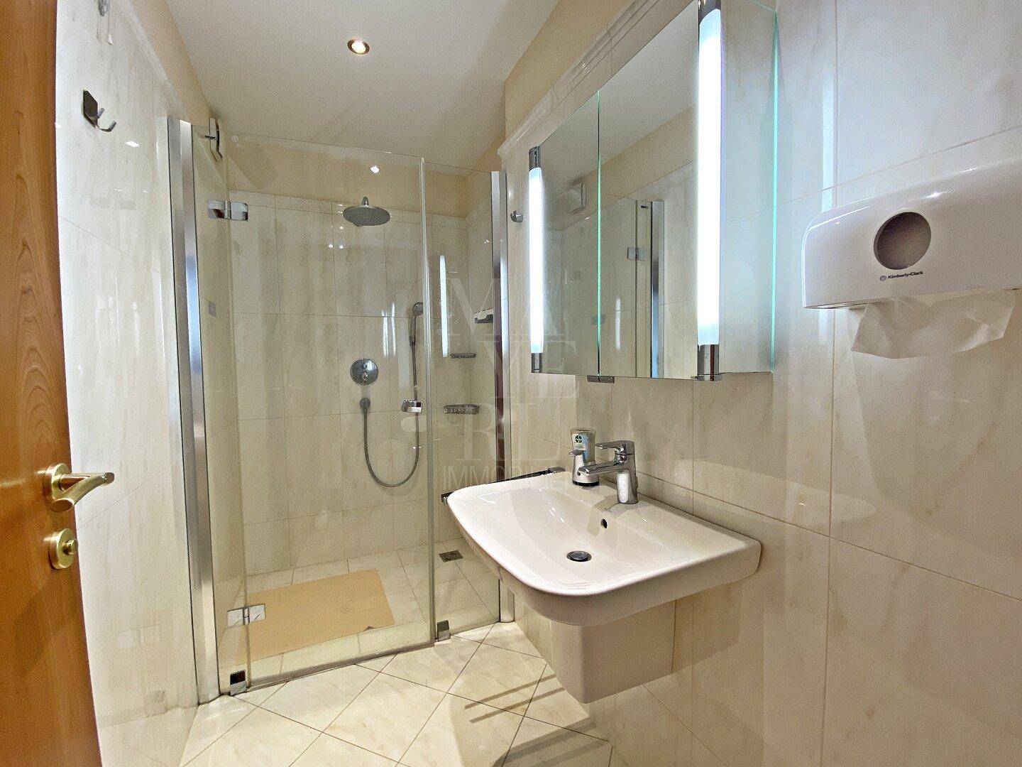 Modernes Badezimmer mit Duschkabine, Einzelwaschbecken und Spiegelschrank, hell gefliest.