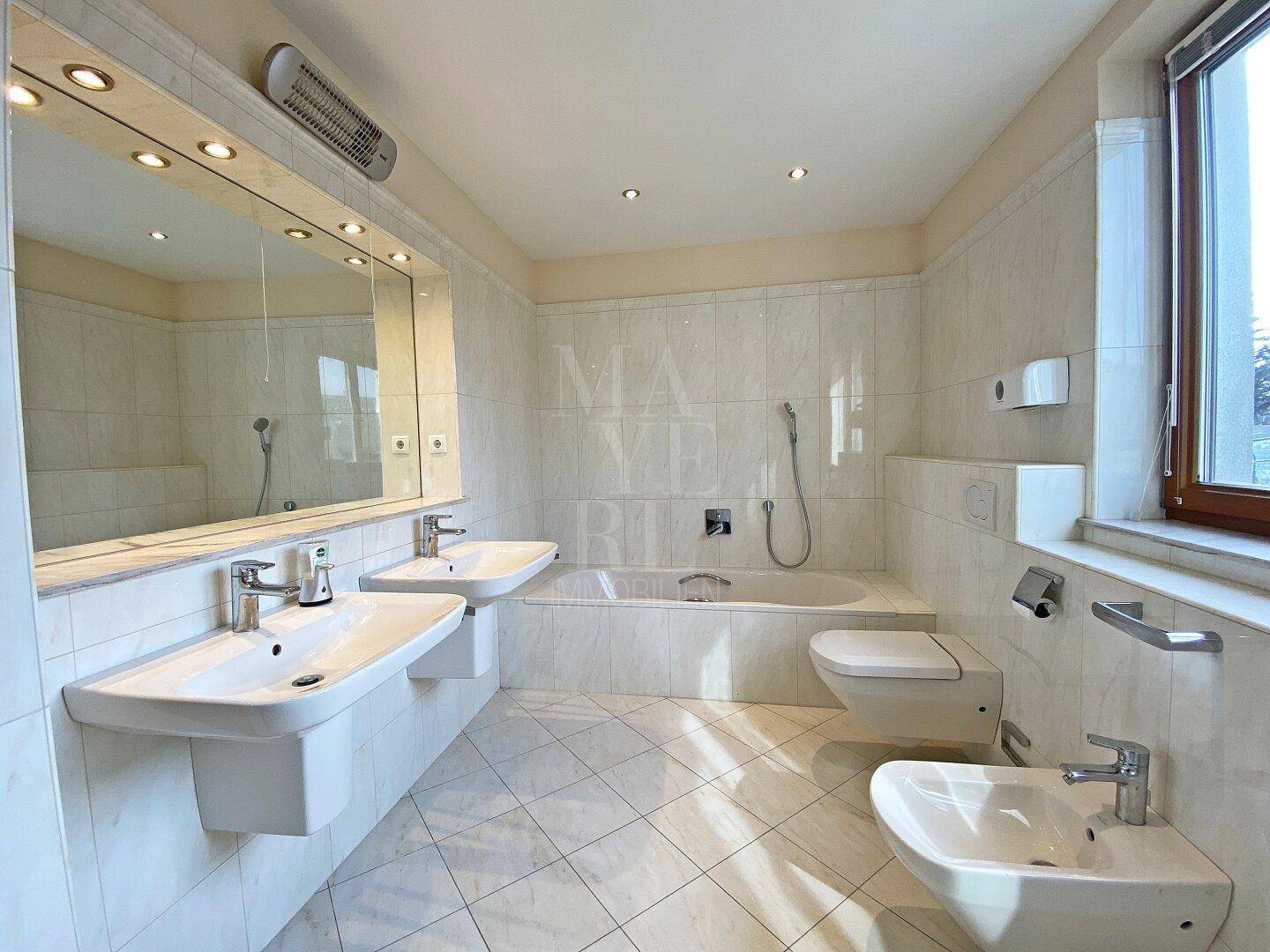 Geräumiges Badezimmer mit Doppelwaschbecken, Badewanne, Bidet und Fenster, hell gefliest.