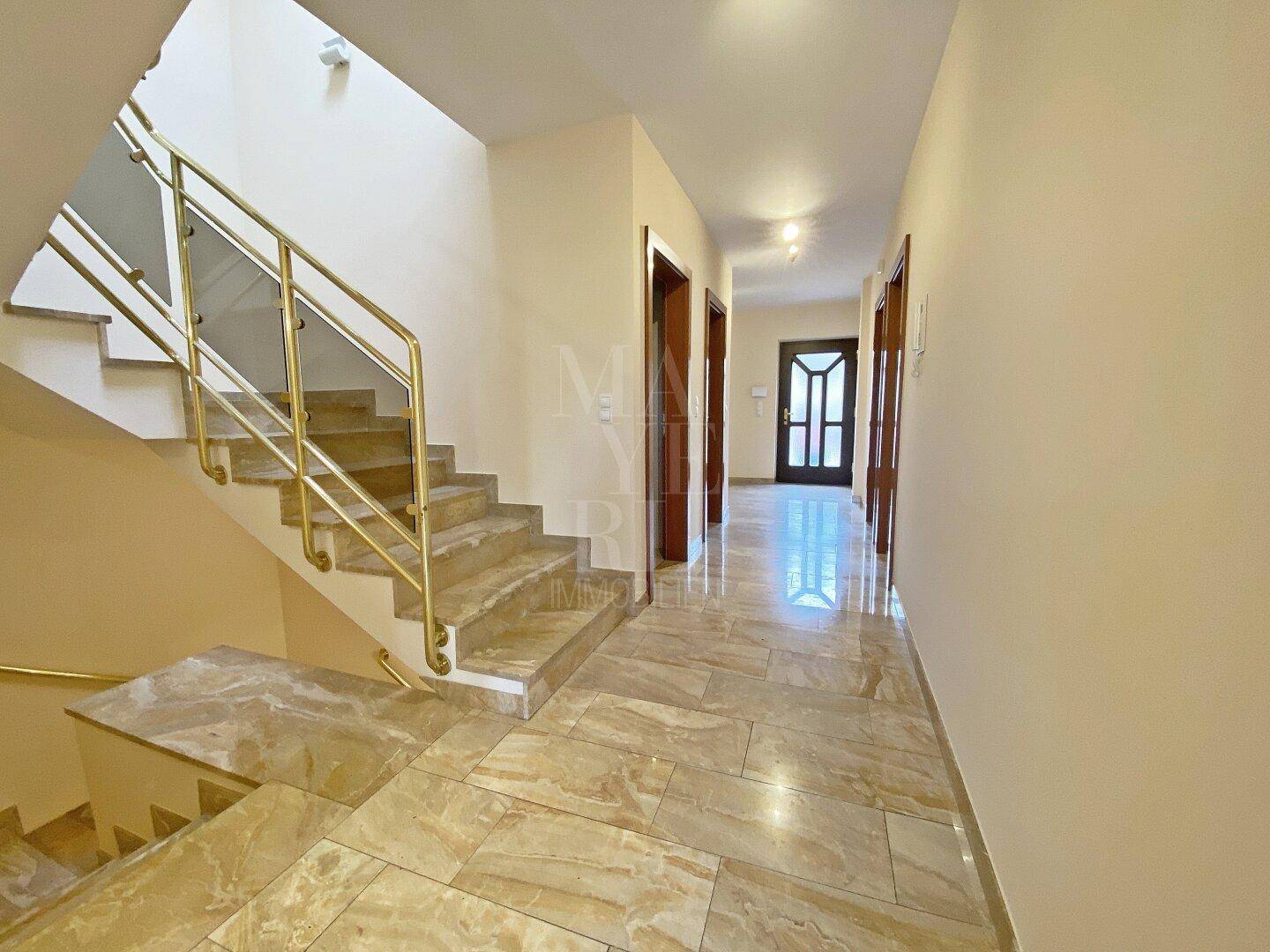 Geräumiger Flur mit eleganter Treppe und glänzendem Fliesenboden, der zu den oberen Etagen führt.