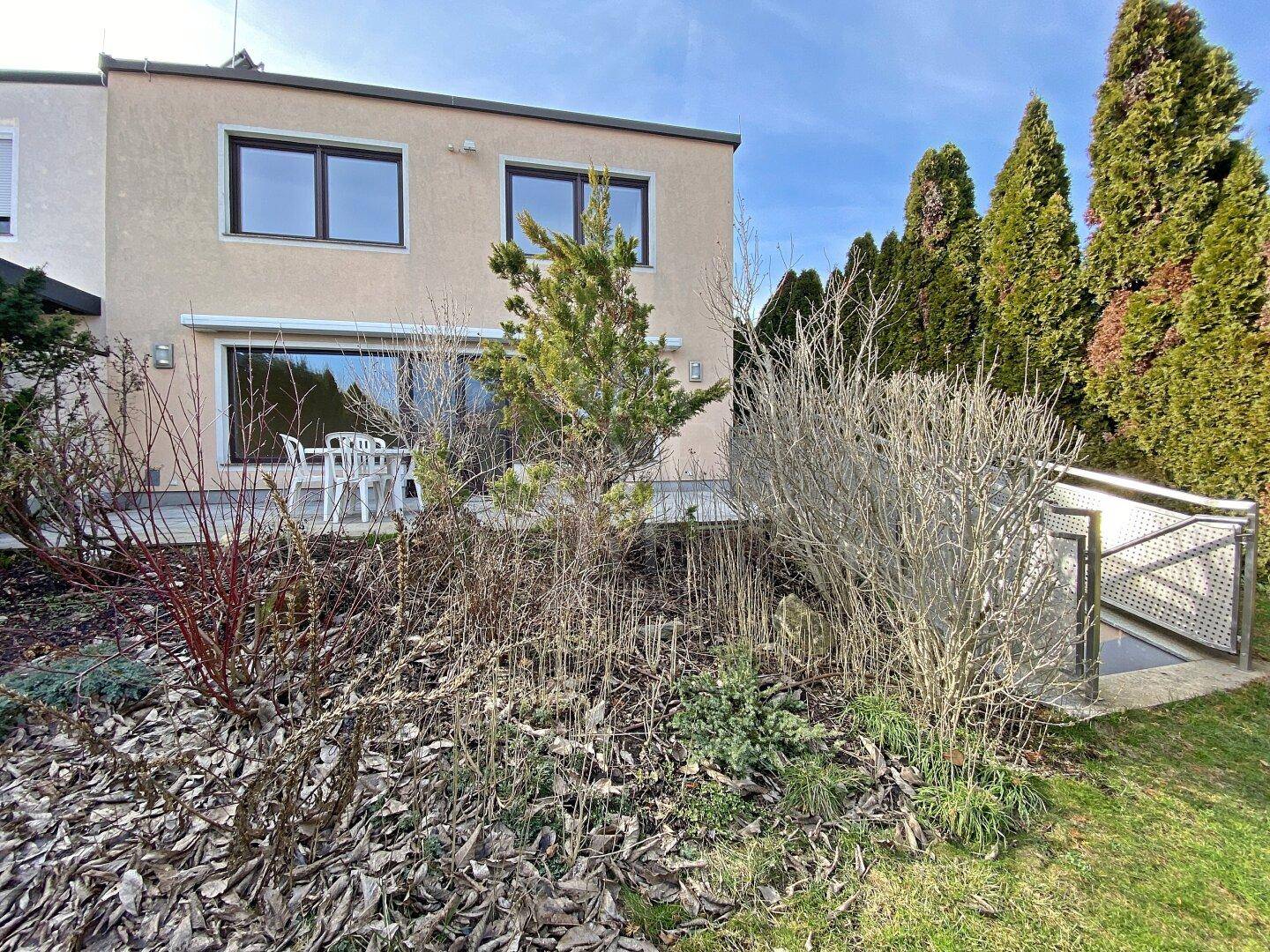 Rückseite des Hauses mit Terrasse, Garten und Zugang zum Keller, umgeben von üppigem Grün.