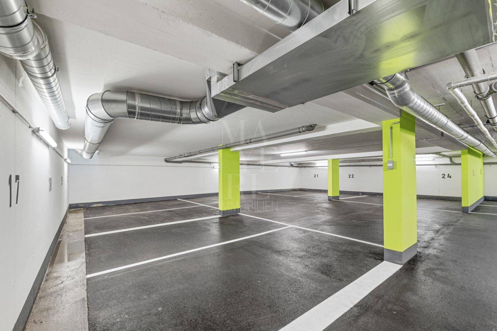 Saubere Tiefgarage mit markierten Parkplätzen, hellgrünen Säulen und industrieller Deckenkonstruktion.