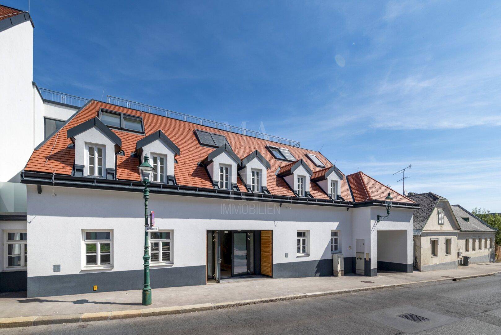 Historisches Gebäude mit rotem Ziegeldach, Gaubenfenstern und weißer Fassade an einer Straße.