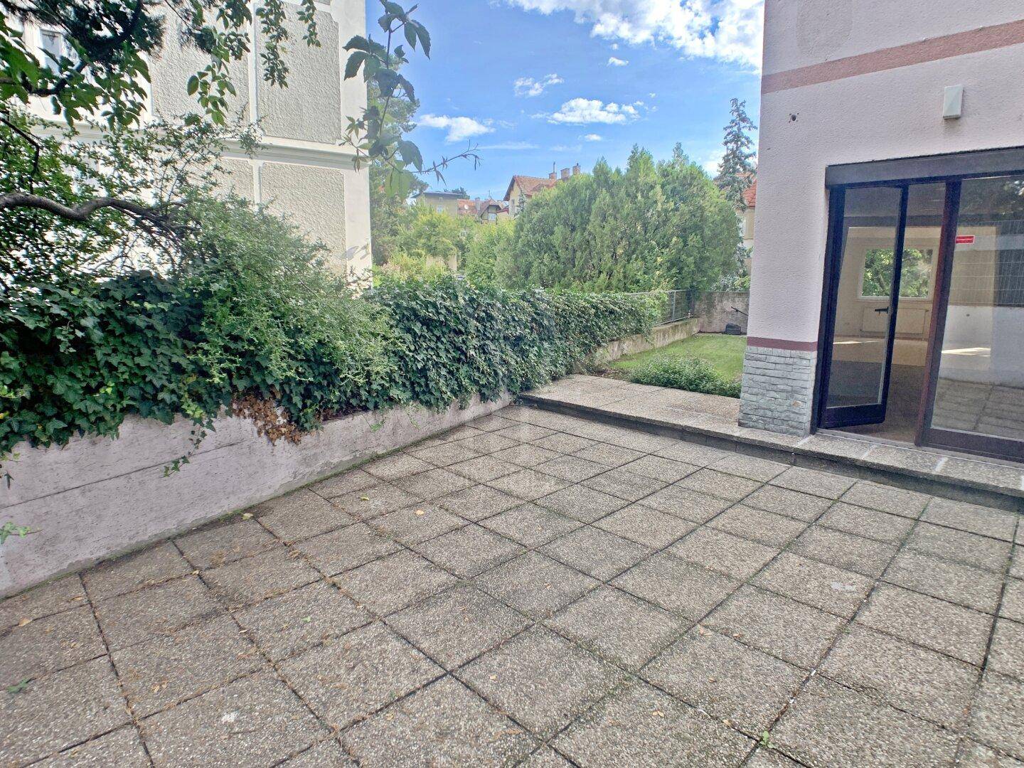 Geräumige Terrasse am Gebäude mit Zugang zum Gartenbereich und grüner Bepflanzung.