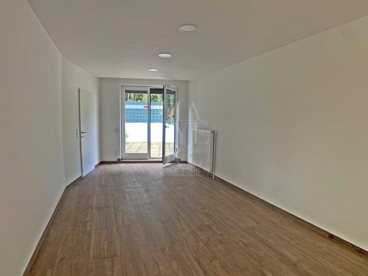 Heller Raum mit Holzboden und direktem Zugang zur Terrasse durch eine Glastür.