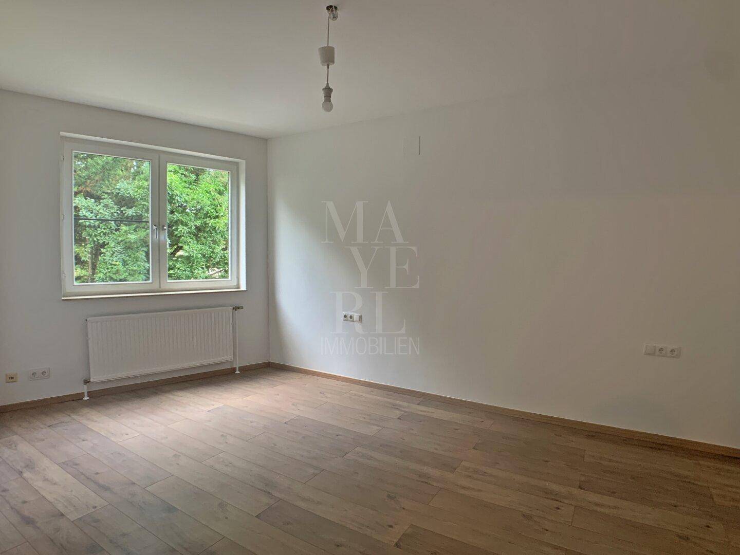 Helles Schlafzimmer mit Holzboden und großem Fenster mit Blick ins Grüne.