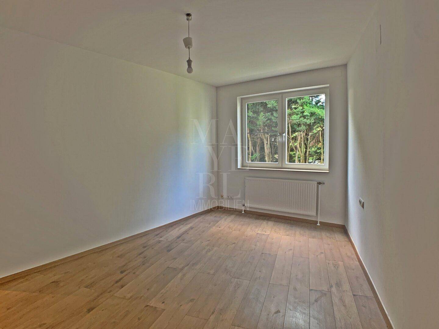 Geräumiges Schlafzimmer mit Holzboden und viel Tageslicht durch das Fenster.