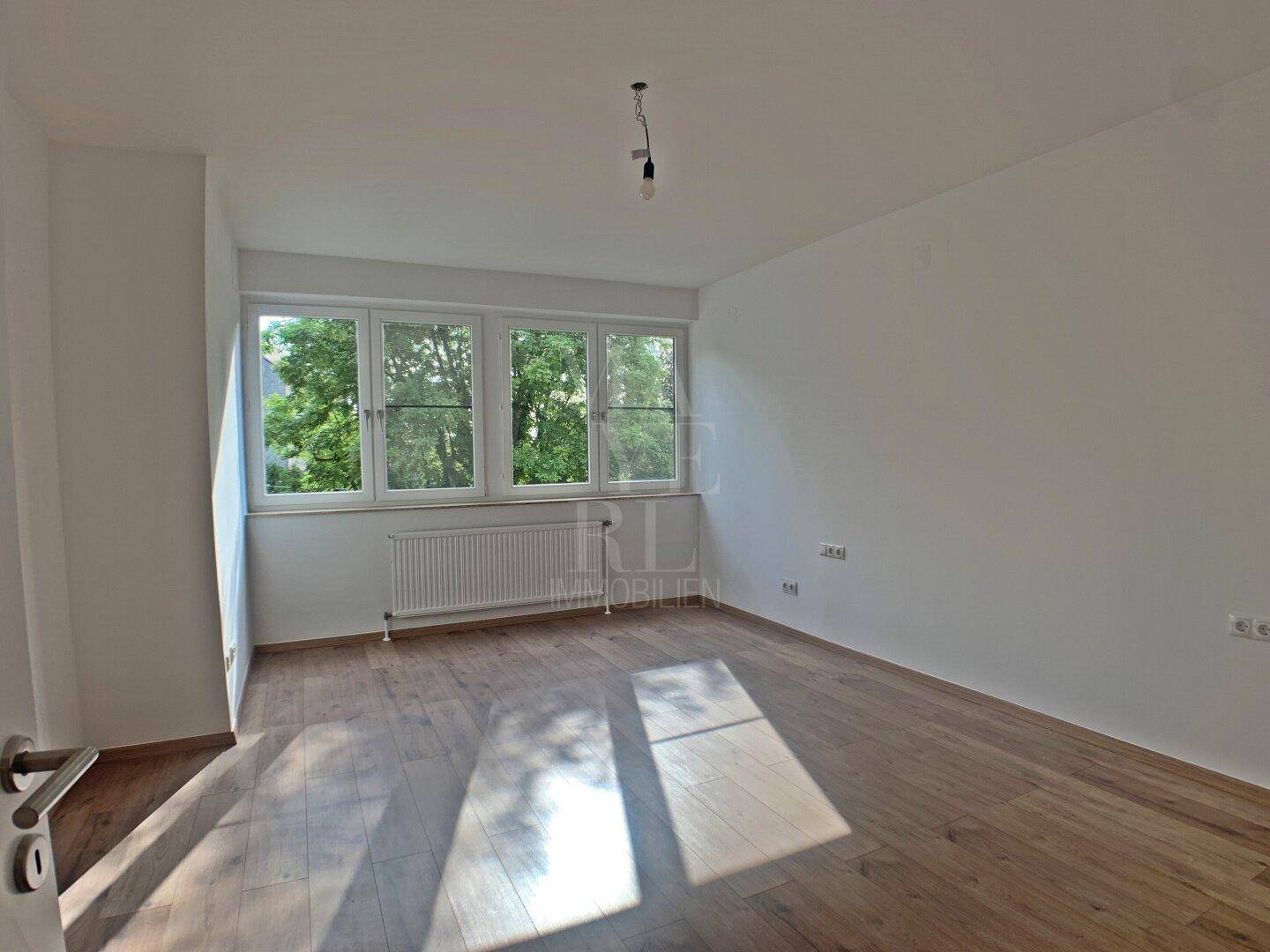 Lichtdurchflutetes Schlafzimmer mit mehreren Fenstern und hellem Holzboden.