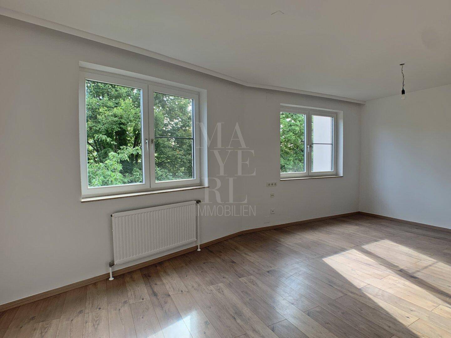 Helles Schlafzimmer mit zwei Fenstern, Holzboden und Blick ins Grüne.